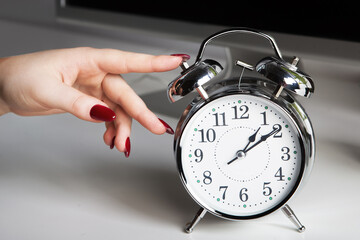 Woman turns off the alarm clock while working at the table with a computer. Working time concept in business people.