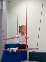 Child on swing during sensory integration session. Little girl in rehabilitation centre doing exercises for development functions of the vestibular apparatus
