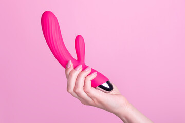 Pink sex toy rabbit shaped vibrator for women in female hand isolated on light pink background - obrazy, fototapety, plakaty