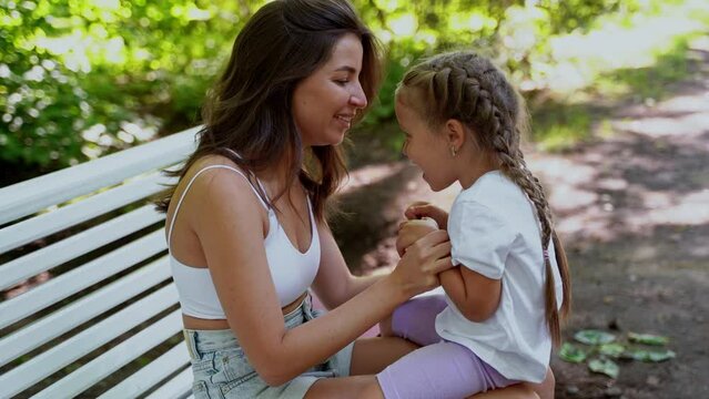 Mother and daughter playing on bench after skating inline roller in public park together. Family leisure sport activity weekend.