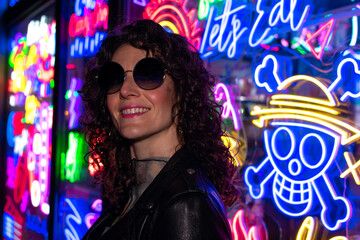 Fashion portrait of a young woman in sunglasses posing near neon signs in night club