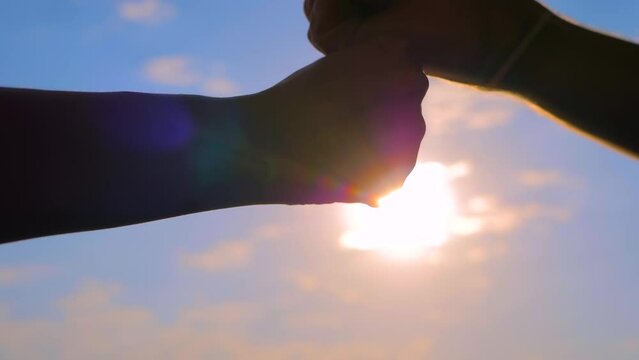Close up shot: silhouettes of man and woman hands are bumping fists against the sunset or sunrise sky - sun lens flares. Informal greeting, agreement, friendship, giving dap and teamwork concept