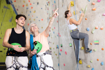 in gym,male male coach encourages mature female client before climbing new difficult route and points to comfortable hooks