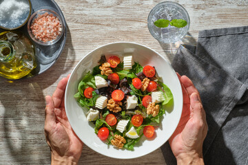 image from above of a man's hands holding a white plate full of healthy fresh salad