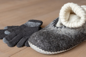 On the wooden floor there are a men's slippers made of dried wool, a handmade woolen sock and gloves in natural color.