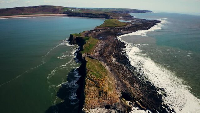 Aerial view of waves crashing onto a rocky coastline at Worm's Head on the Gower peninsula of Wales