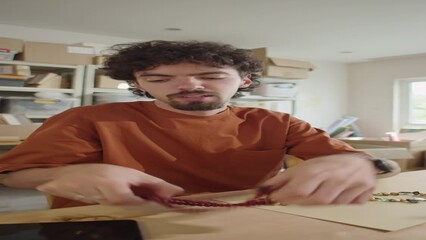 Vertical POV shot of young man demonstrating handmade beaded jewelry and talking on camera while filming DIY blog or video advertising for online store