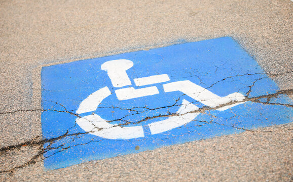 The blue handicap sign on the street is a universal symbol for accessibility and mobility aid for individuals with disabilities, representing equal opportunities and inclusion