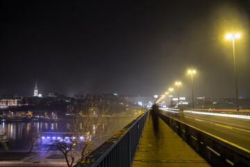 Fototapeta na wymiar BELGRADE, SERBIA - FEBRUARY 27, 2015: Dark shapes of people walking on Brankov Most (Branko's Bridge) at night with Belgrade (skyline in the background. Brankov Most is one of the main bridges on Sava