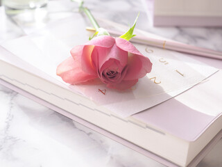 大理石の女性らしいデスク、ピンクのノートと一輪のバラの花