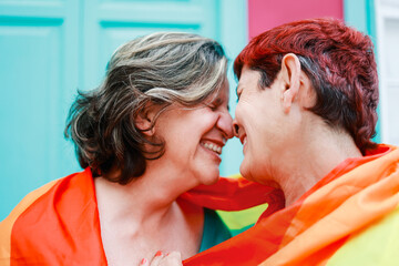 Happy gay senior lesbian couple wearing lgbt rainbow flag outdoors - Diversity family love - Main focus on right woman head