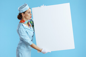surprised stylish female stewardess on blue showing blank board