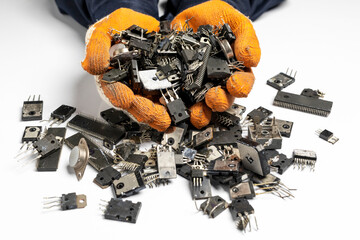 Broken electronic components, ICs, transistors and diodes, in hand, on a white background.