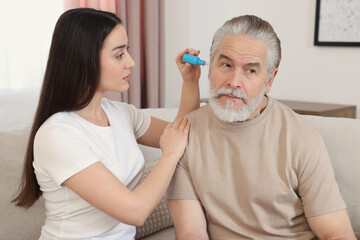 Young woman dripping medication into man's ear at home