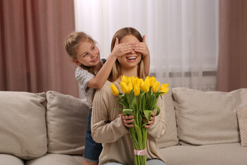 Little daughter congratulating mom with bouquet of yellow tulips at home. Happy Mother's Day