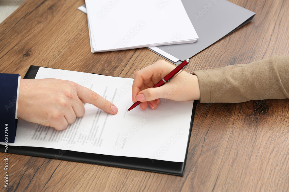 Wall mural Man pointing at document and woman putting signature at wooden table, closeup