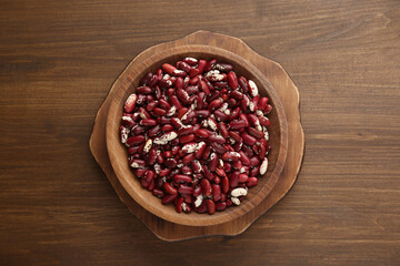Bowl with dry kidney beans on wooden table, top view