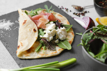 Delicious pita wrap with jamon, cheese cream and greens on light gray table, closeup