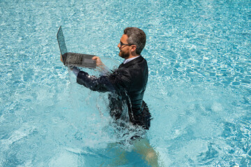 Business man in suit working on laptop in swimming pool. Travel tourism and business concept. Crazy...