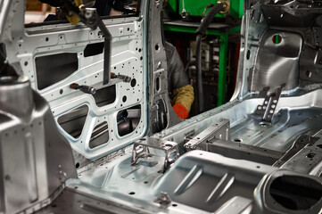 Laborer welds manually steel parts of car body in workshop