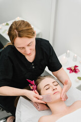 Obraz na płótnie Canvas Cosmetologist making rejuvenating face procedures client in spa salon. Gua Sha, gouache scraper device for face massage treatment. Aesthetic cosmetology, face care. Facial treatment, skincare concept.