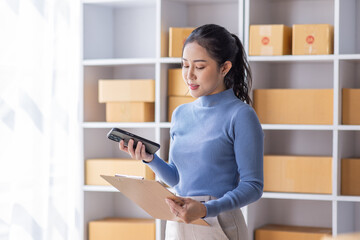 Portrait of Starting Asian female small businesses owners SME entrepreneur working at Laptop in home Warehouse, online marketing, packing boxes, SME sellers, concept, e-commerce team, online sales.	