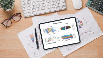 Tablet with financial charts and reports on office desk workplace. Top view flat lay.