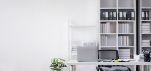 Laptop Computer, notebook, and eyeglasses sitting on a desk in a large open plan office space after...