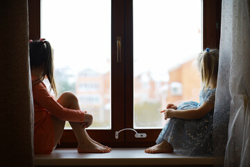 Beautiful little girl smiling and watching out the window. A child looks out the window. Young girl looking from window.