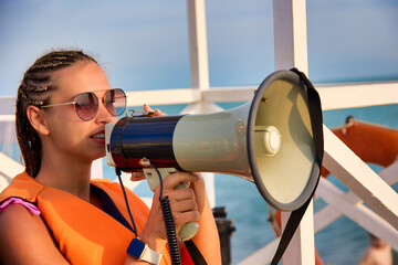 Young woman with fashionable modern hairstyle on head in an orange life jacket poses with megaphone...