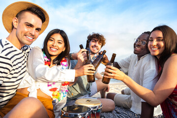 Happy multiracial group of friends toasting with beer together at beach picnic party looking at camera.