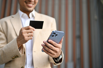 Close-up image of a happy Asian businessman holding a business card and his smartphone.