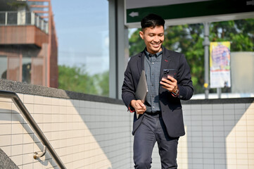 Busy Asian businessman checking messages on his phone while walking out of the metro train station