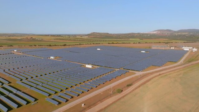 Aerial side pan of giant solar plant on aride plain, sunny day 