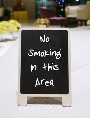 small black chalkboard in the building lobby table written NO SMOKING IN THIS AREA  , concept of warning sign to remind customers or visitos not to smoke in public area