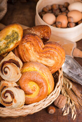 Flour products of various types. Wicker basket with different types of bread and sweet buns on a wooden table.