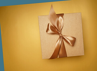 Surprise, gift. top view of small gift box tied with golden ribbon on yellow background