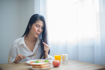 Obraz na płótnie Canvas Beautiful asian woman eating a plate of fried eggs and fresh green vegetables with happiness.