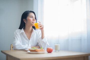 Beautiful asian woman savored her glass of juice while gazing into the copy space with breakfast on the table.