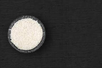 White rice in a rustic stone bowl on a black wooden background