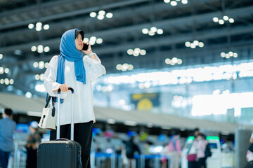 An Asian Muslim wearing a blue hijab is preparing for a vacation and she is at the airport. She is using her mobile phone to contact her friends and Muslim travelers.