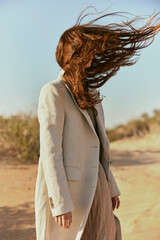 portrait of a woman in a light jacket with hair covering her face from the wind