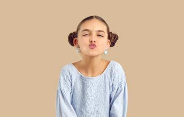 Portrait of lovely funny cute kid girl making air kiss on camera on beige studio background. Beautiful stylish caucasian preteen girl with hairstyle with two bundles makes lips for kiss. Banner.