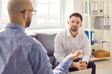Business people meeting in the office. Young man sitting on the sofa and listening to his business agent, colleague or financial partner talking about work