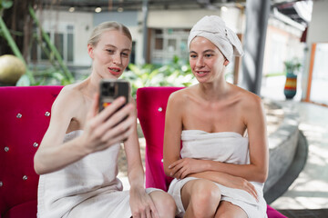 Relaxed two Caucasian woman use smart phone with therapist in spa salon