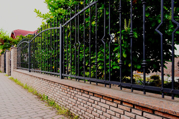 decorative wrought iron picket fence panels between stucco finished piers. green garden with lush...