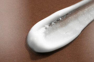 Sample of white cream on a dark brown background. Close-up of lotion smear, foam macro.