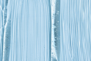 Transparent gel texture with bubbles and particles for cleansing close-up on a blue background, top view. Beauty background macro.