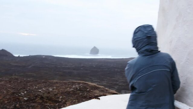 Woman tourist stand by building hold on hardly can stand in extreme Icelandic weather in south coast by atlantic ocean. Travel Iceland changeable weather and high winds forecasts