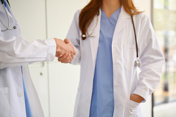 A professional female doctor shakes hands with her colleagues in a hospital corridor.